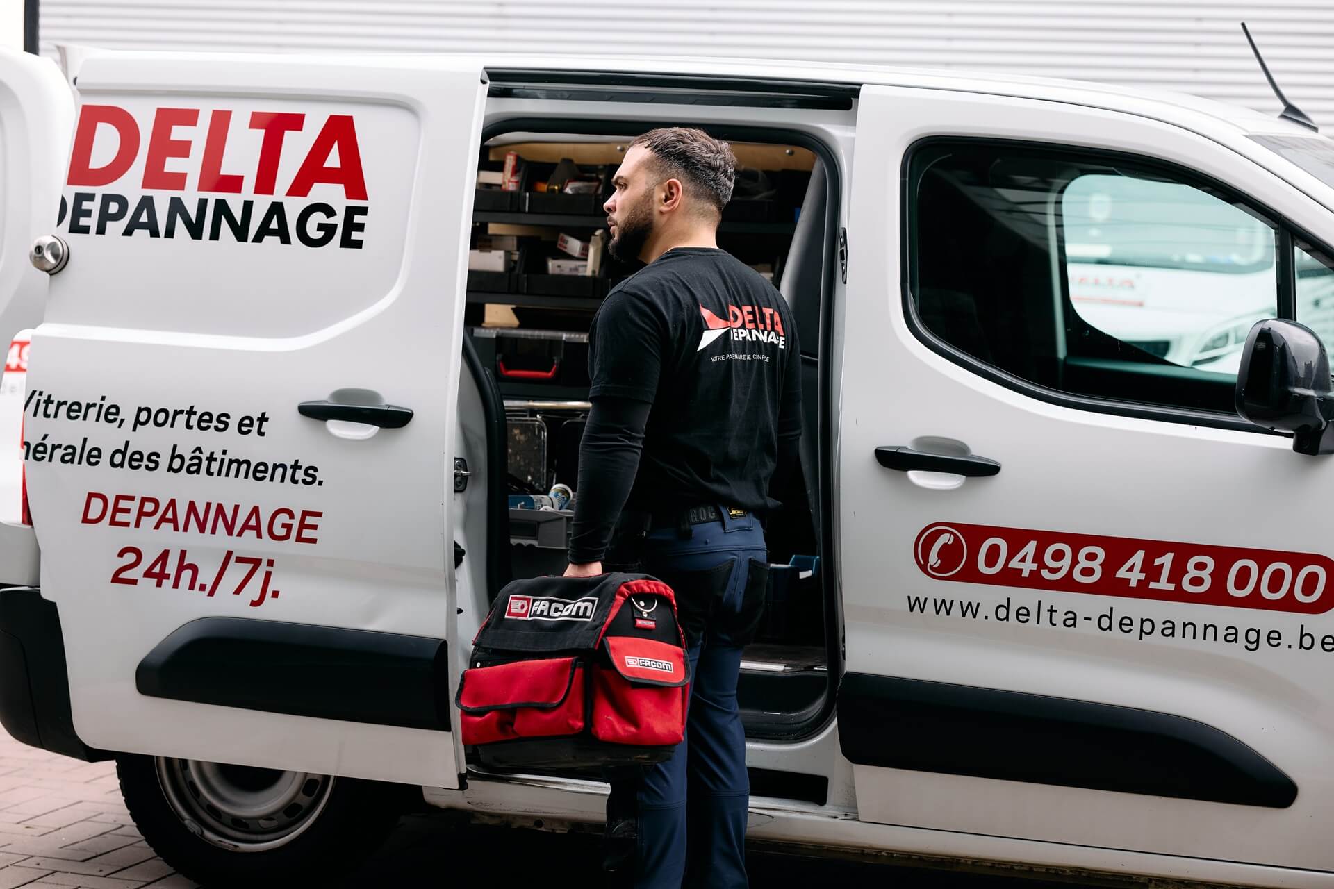 Un employé de Delta Dépannage se trouve devant leur camionnette avec un sac à outils.